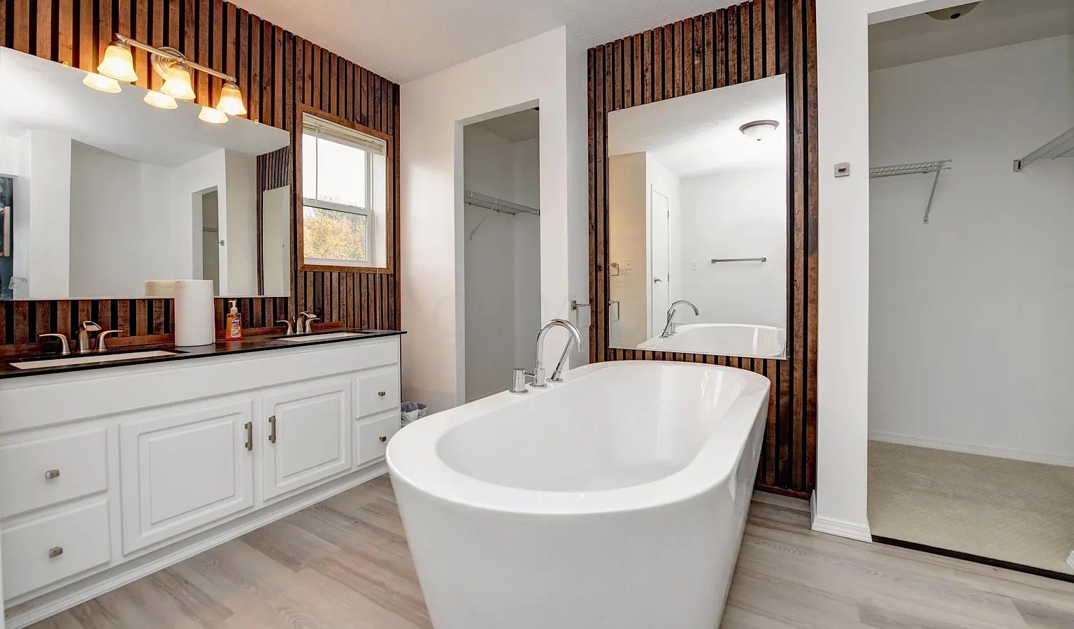 Primary bathroom with a freestanding white tub in front of a vertical reclaimed-wood wall