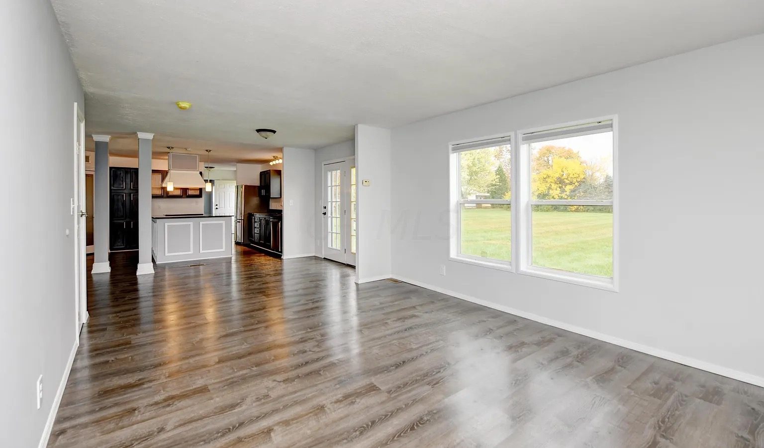 Open great room with white wainscot panelling, wide-plank floors, and columns opening to the kitchen
